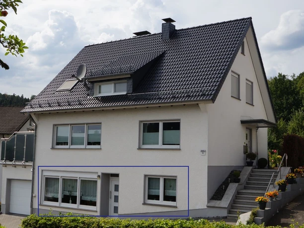 Aussenansicht Zweistöckiges Wohnhaus mit grauem Dach, weißen Wänden, mehreren Fenstern und seitlichen Treppen.