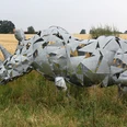 Skulptur Nashorn Metallische Nashornskulptur mit geometrischen Formen steht auf einer Wiese vor einem Getreidefeld.