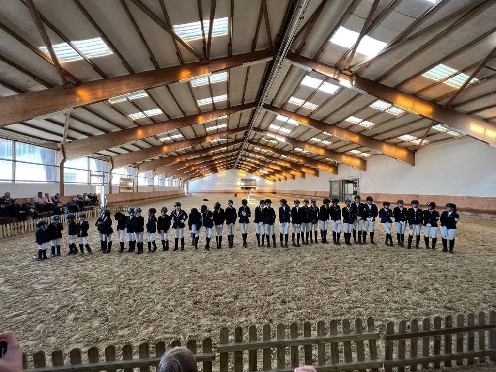 Reithalle von ReitsportKonzepte Völker in Haan Reiterinnen und Reiter stehen nebeneinander in einer großzügigen, holzgetäfelten Reithalle in Haan.