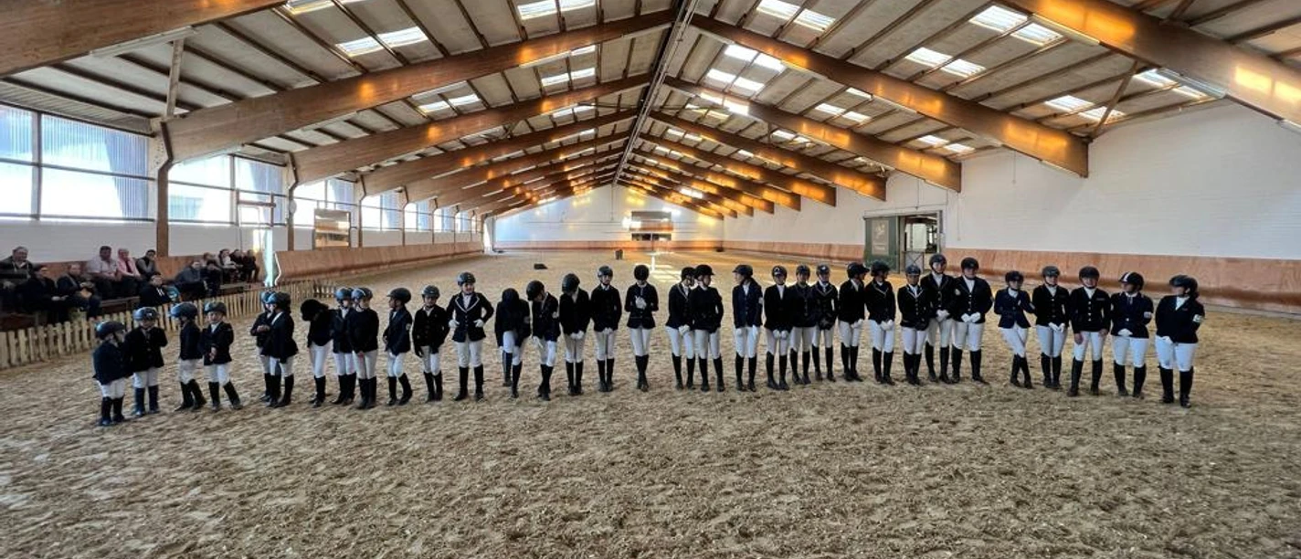 Reithalle von ReitsportKonzepte Völker in Haan Reiterinnen und Reiter stehen nebeneinander in einer großzügigen, holzgetäfelten Reithalle in Haan.