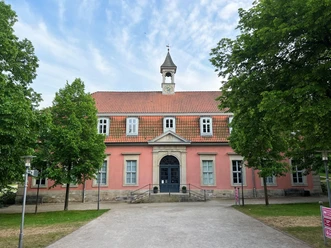 The building with its rose facade and bell tower, surrounded by trees, has a calm and appealing appearance.