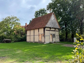 Pastorenhaus Marfeld Fachwerkhaus mit holzgedecktem Dach umgeben von grüner Wiese und Bäumen bei Sonnenlicht.