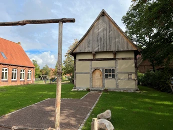 Historisches Fachwerkgebäude in ländlicher Umgebung mit gepflegtem Rasen und umgebenden Bäumen.