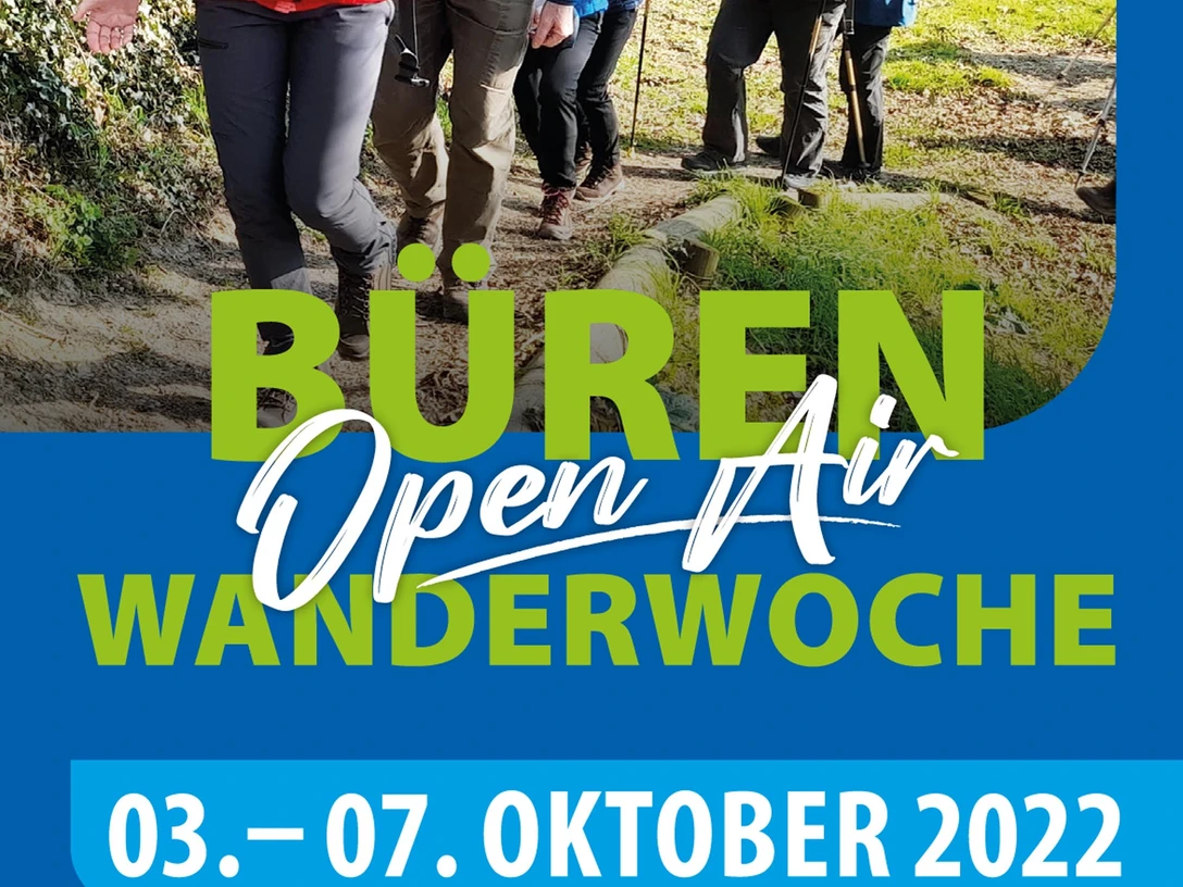 Bueren_Flyer_Wanderwoche_2022 - final-1.jpg Gruppe fröhlicher Wanderer auf einem sonnigen Waldweg, flankiert von Bäumen und Wiese.