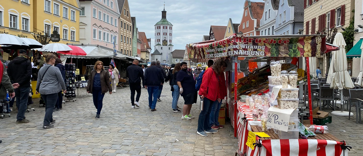 Maimarkt in Günzburg Maimarkt in Günzburg: Menschen flanieren auf belebtem Markt mit bunten Ständen und historischen Gebäuden.