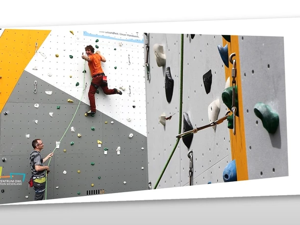 Kletterer erklimmt bunte Kletterwand, abgesichert durch eine Person am Boden, die Seil sichert.