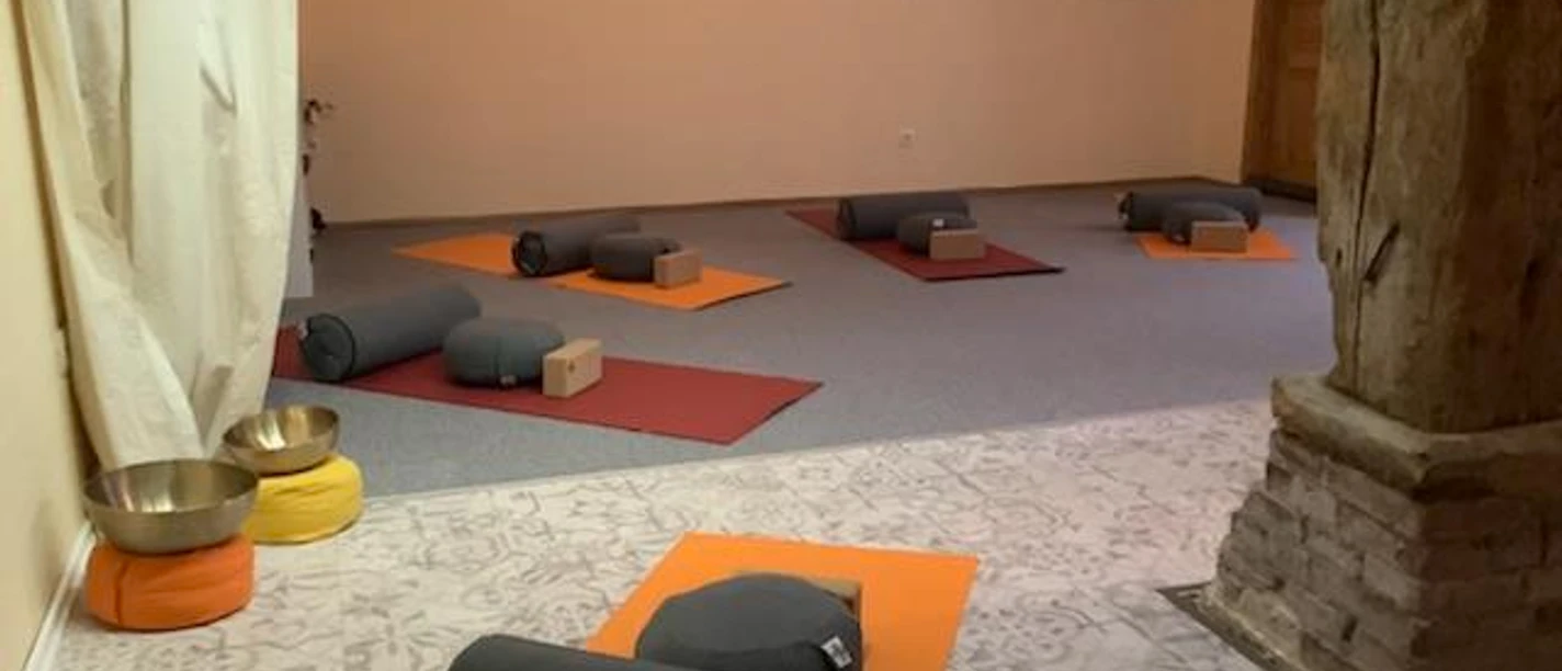 Yoga in der Natur-Klang-Raum Praxis im Spiegelhaus Woltzeten Yogaraum mit Matten, Bolstern und Klangschalen, sanft beleuchtet für Meditation und Entspannung.