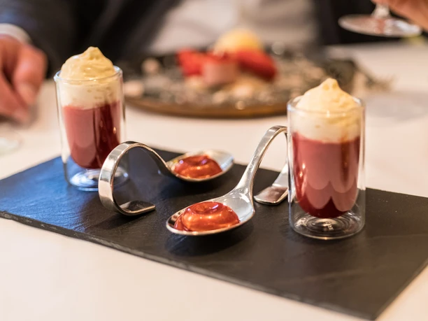 Hotel Zur Post Zwei Gläser mit roter Mousse und Sahne, serviert auf elegantem Tablett mit dekorativen Löffeln.