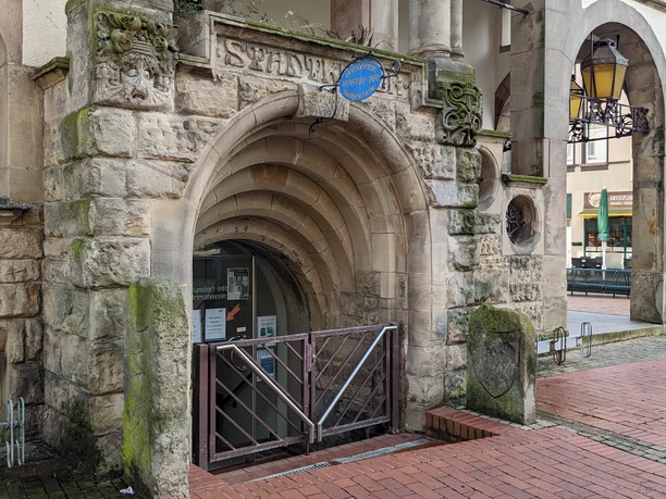 WunstorfInfo01.jpg Historischer Eingang zur Stadtbücherei mit Rundbogen und alten Steinverzierungen in einer urbanen Umgebung.