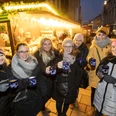 Lübbecker Weihnachtsmarkt Eine Gruppe von sieben Personen hält Tassen mit Glühwein, fröhlich vor einem Weihnachtsmarktstand.