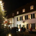 Weihnachtsmarkt mit beleuchtetem Tannenbaum vor historischem Gebäude, umgeben von Besuchern bei Nacht.