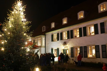 Weihnachtsmarkt Haus des Gastes Weihnachtsmarkt mit beleuchtetem Tannenbaum vor historischem Gebäude, umgeben von Besuchern bei Nacht.