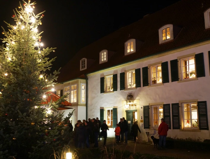 Weihnachtsmarkt Haus des Gastes Weihnachtsmarkt mit beleuchtetem Tannenbaum vor historischem Gebäude, umgeben von Besuchern bei Nacht.