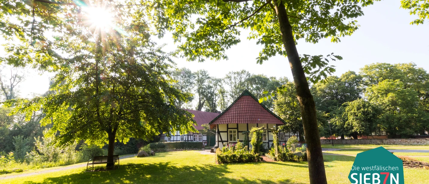 Hille Traditionelles Fachwerkhaus im dichten grünen Wald, direkte Sonne im Hintergrund, ruhig gelegen.