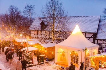 Stemwede-Levern Weihnachten Weihnachtsmarkt in Stemwede-Levern bei Schneefall, mit Lichtern, Ständen und einem weißen Zelt.
