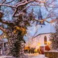 Stemwede-Levern Weihnachten Verschneiter Kirchenplatz in Stemwede-Levern, umgeben von Fachwerkhäusern, Lichterketten funkeln.