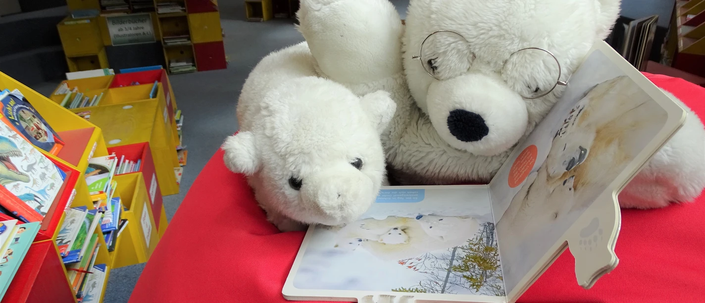 Bilderbücher entdecken © Stadtbibliothek Lingen.JPG Zwei Plüsch-Eisbären lesen gemeinsam ein Kinderbuch in der bunten Leseecke einer Bibliothek.