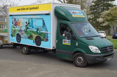 Spielmobil Hilden Ein grüner Lieferwagen des Spielmobils Hilden mit buntem Grafitti parkt auf einer Straße.