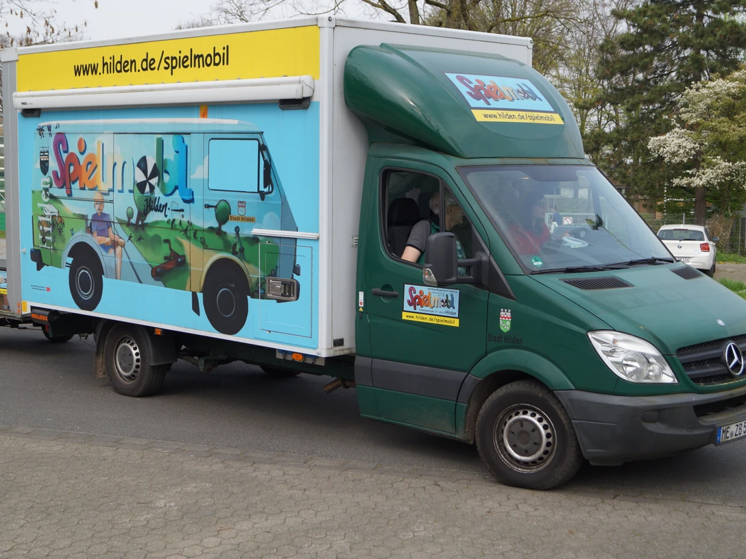 Spielmobil Hilden Ein grüner Lieferwagen des Spielmobils Hilden mit buntem Grafitti parkt auf einer Straße.