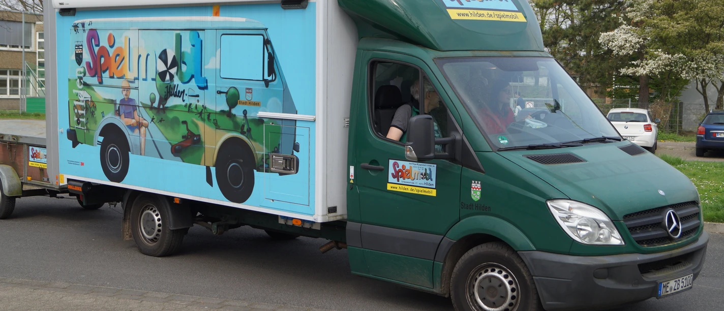 Spielmobil Hilden Ein grüner Lieferwagen des Spielmobils Hilden mit buntem Grafitti parkt auf einer Straße.