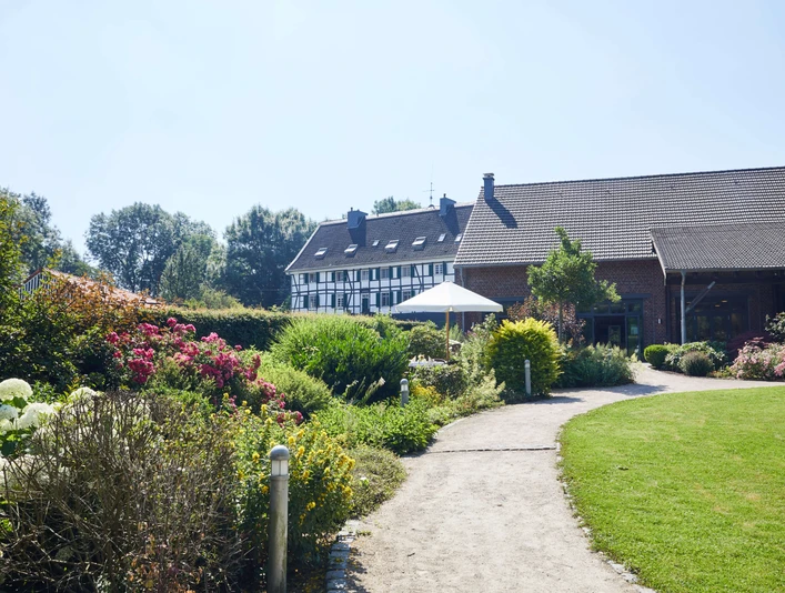 Privatunterkunft Wolff am Abtskücher Teich in Heiligenhaus Gemütliches Backsteinhaus mit gepflegtem Garten, umgeben von üppiger Natur, im Sommerlicht.