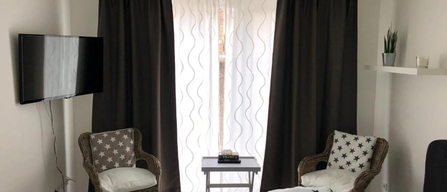 Pension Osthoff Wülfrath Zimmer der Pension Osthoff Wülfrath mit modernen Möbeln, TV, zwei Stühlen und dunklen Vorhängen.