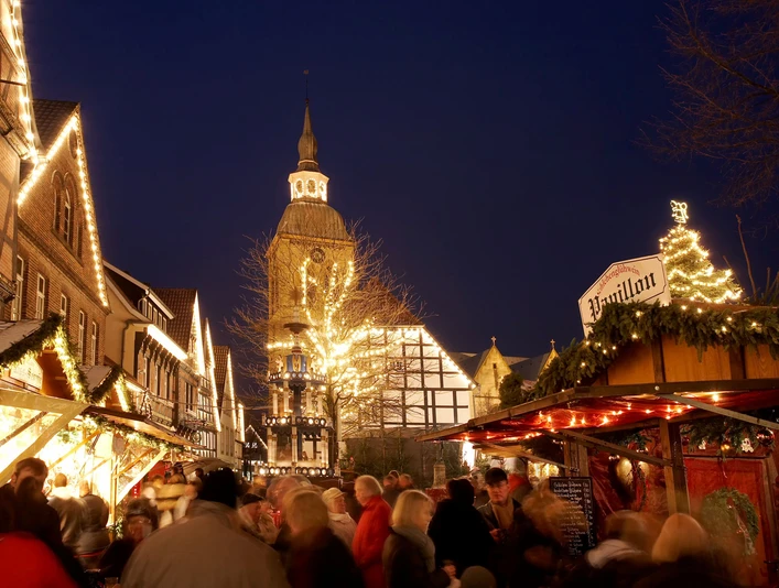 Ein festlich beleuchteter Weihnachtsmarkt bei Nacht mit Menschenmenge und historischer Kirche im Hintergrund.