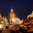 Christkindlmarkt Wiedenbrück Ein festlich beleuchteter Weihnachtsmarkt bei Nacht mit Menschenmenge und historischer Kirche im Hintergrund.