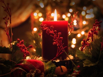 Rote Kerze im Vordergrund auf festlichem Adventskranz, umgeben von roten Beeren und weihnachtlichem Glanz.