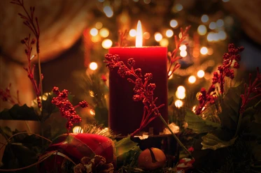 Konzert bei Kerzenschein Rote Kerze im Vordergrund auf festlichem Adventskranz, umgeben von roten Beeren und weihnachtlichem Glanz.