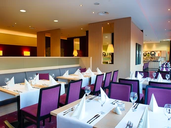 Welcome Hotel Paderborn / Restaurant Paderaue Innenansicht eines modernen Restaurants mit gedeckten Tischen, violetten Stühlen und warmem Licht.