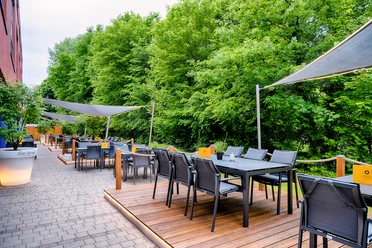 Sonnige Terrasse mit modernen Sitzmöbeln im Schatten von Markisen und umgeben von grünem Laubwerk.