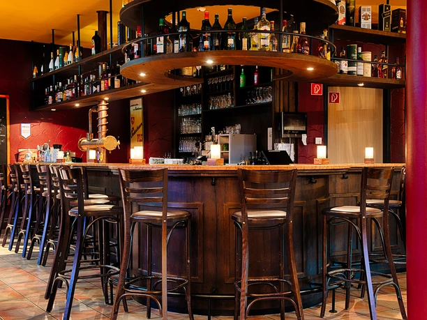 Eine einladende Bar in warmen Farbtönen mit Holzhockern und Regalen voll bunter Flaschen.