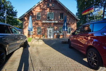 bei-nico-griechisches- restaurant-amelinghausen.jpg Rotes Backsteingebäude des griechischen Restaurants Bei Nico mit Parkplatz und Flaggen.