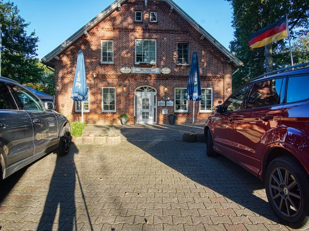 bei-nico-griechisches- restaurant-amelinghausen.jpg Rotes Backsteingebäude des griechischen Restaurants Bei Nico mit Parkplatz und Flaggen.