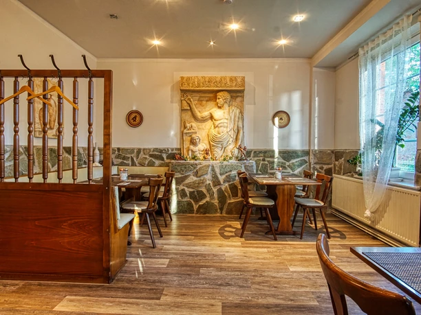 bei-nico-griechisches- restaurant-amelinghausen-innen.jpg Heller Gastraum mit Holztischen, Steinwandverkleidung und griechischem Wandrelief.