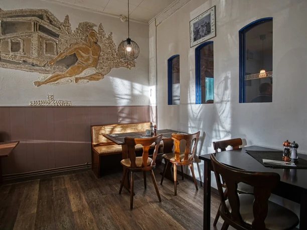 bei-nico-griechisches- restaurant-amelinghausen-innen Innenraum mit Holztischen, Stühlen und Wandrelief im antiken Stil in einem Restaurant.