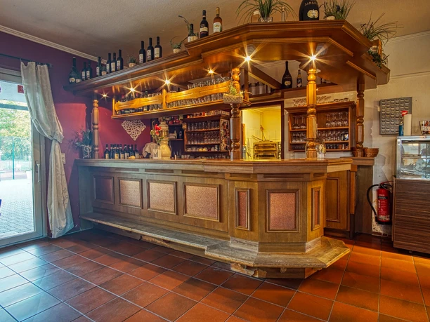 Innen- Restaurant Trattoria da Totti Rustikale Holztheke mit Getränkeregalen und Blick durch die Glastür auf den Tennisplatz.