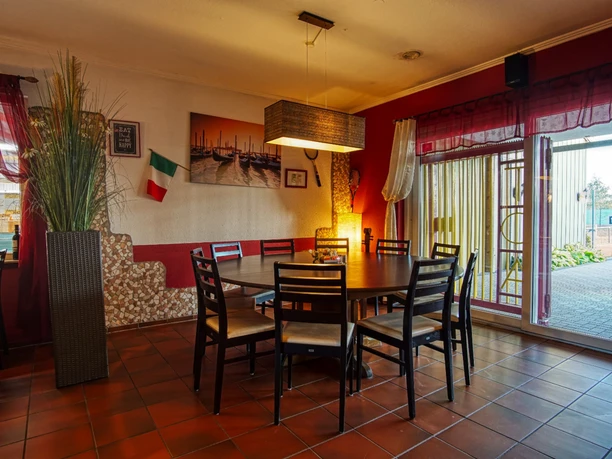 Gastraum der Trattoria Runder Holztisch mit Stühlen im Gastraum der Trattoria mit Blick auf die Außenplätze.
