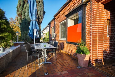 Außenterrasse des Restaurants Terrazza Außenterrasse des Restaurants mit Tisch, dunklen Stühlen, Sonnenschirm vor roter Backsteinfassade.
