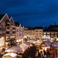 Ein Markt mit festlich beleuchteten Ständen auf einem Platz, umgeben von historischen Gebäuden bei Nacht.