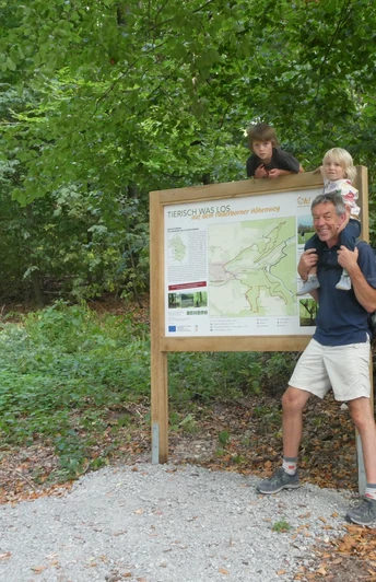 Auf der Familienvariante des Paderborner Höhenwegs Eine Familie posiert vor einer Infotafel, umgeben von üppigem Wald, auf einem Wanderweg.