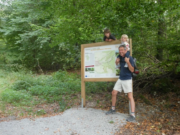 Auf der Familienvariante des Paderborner Höhenwegs Eine Familie posiert vor einer Infotafel, umgeben von üppigem Wald, auf einem Wanderweg.