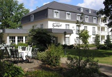 Waldhotel Nachtigall / Außenansicht Weiße Fassade eines dreistöckigen Hotels mit grauem Dach; begrünter Hof und Terrassenbestuhlung.