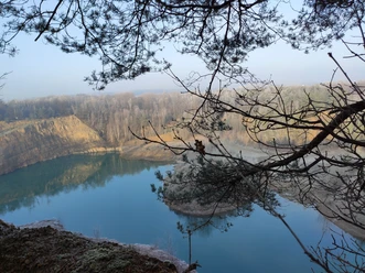 Geopark met meer en bomen, rustig wateroppervlak en beboste oevers op de achtergrond.