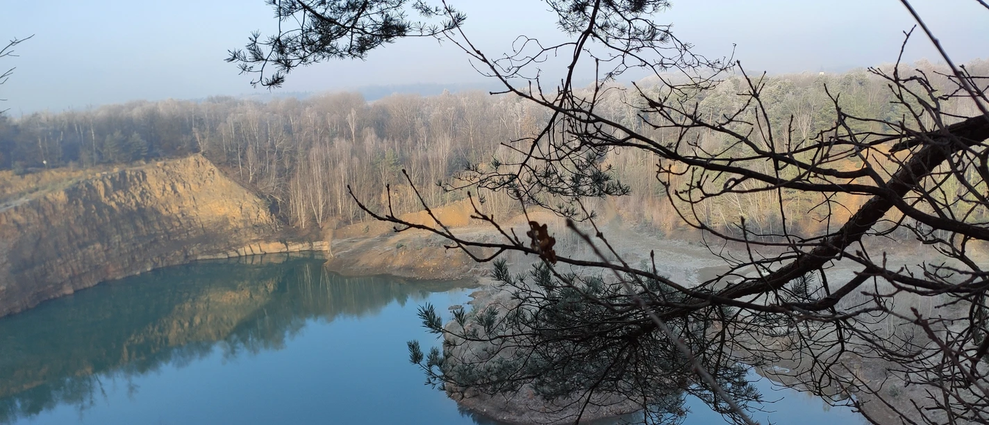 Steinbruch mit See Geopark with lake and trees, calm water surface and wooded banks in the background.