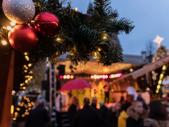 Gütersloher Weihnachtsmarkt Weihnachtlich geschmückter Markt bei Dämmerung mit leuchtenden Kugeln, Lichtern und Menschenmenge.