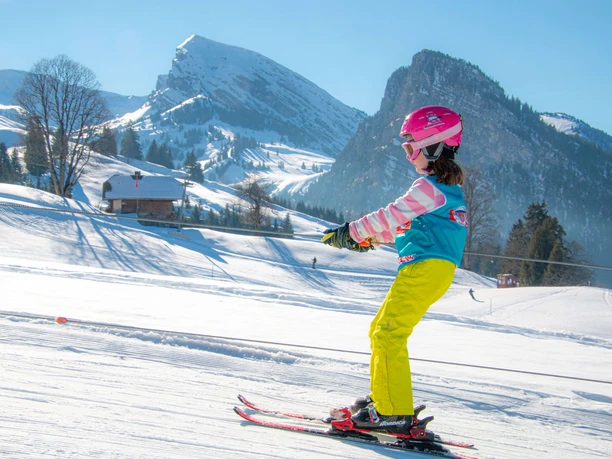 Kinderlift auf Springenboden Kind fährt mit Kinderschlepplift auf Skis den Berg hoch, Bergpanorama im Hintergrund