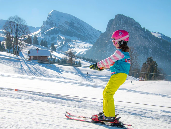 Kinderlift auf Springenboden Kind fährt mit Kinderschlepplift auf Skis den Berg hoch, Bergpanorama im HintergrundChild riding up the mountain on skis with a children's drag lift, mountain panorama in the backgroundUn enfant monte la montagne à ski avec le téléski pour enfants, panorama de montagne en arrière-plan