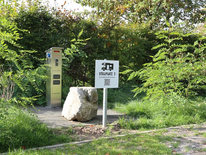 Stellplatz für Wohnmobile mit elektrischem Anschluss, umgeben von grünen Büschen und Bäumen.